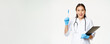 Smiling asian female doctor raising pen up, eureka gesture, holding clipboard, standing in medical uniform over white background