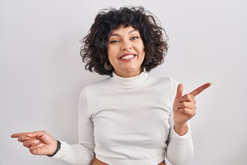 Hispanic woman with curly hair standing over isolated background smiling confident pointing with fingers to different directions. copy space for advertisement