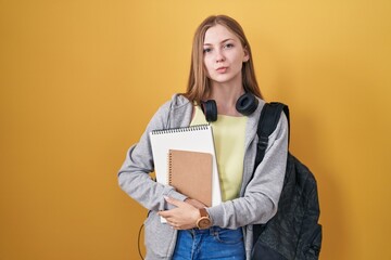 Canvas Print - Young caucasian woman wearing student backpack and holding books looking at the camera blowing a kiss on air being lovely and sexy. love expression.