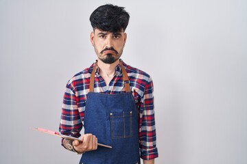 Sticker - Young hispanic man with beard wearing waiter apron holding clipboard depressed and worry for distress, crying angry and afraid. sad expression.