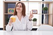 © Krakenimages.com - Brunette woman drinking glass of orange juice smiling looking to the camera showing fingers doing victory sign. number two.