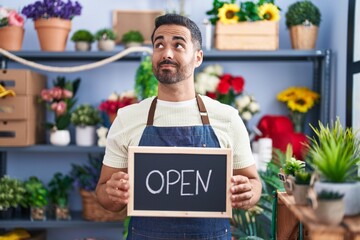 Sticker - Hispanic man with beard working at florist holding open sign smiling looking to the side and staring away thinking.