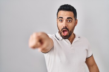 Canvas Print - Young hispanic man with beard wearing casual clothes over white background pointing with finger surprised ahead, open mouth amazed expression, something on the front