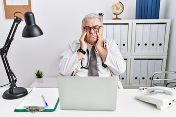 Canvas Print - Senior caucasian man wearing doctor uniform and stethoscope at the clinic with hand on head, headache because stress. suffering migraine.