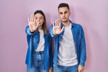 Young hispanic couple standing over pink background doing stop sing with palm of the hand. warning expression with negative and serious gesture on the face.