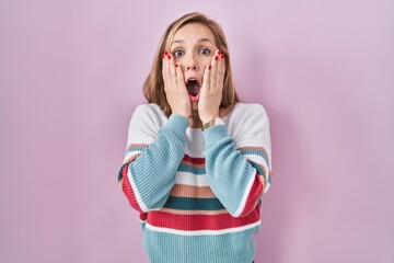 Canvas Print - Young blonde woman standing over pink background afraid and shocked, surprise and amazed expression with hands on face