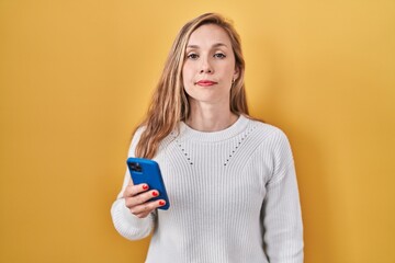 Wall Mural - Young blonde woman using smartphone typing message relaxed with serious expression on face. simple and natural looking at the camera.