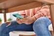 Young hispanic woman using smartphone under table at home