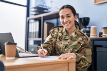 Young Hispanic Woman Army Soldier Using Laptop Writing On Document At Office