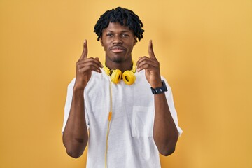 Sticker - Young african man with dreadlocks standing over yellow background pointing up looking sad and upset, indicating direction with fingers, unhappy and depressed.