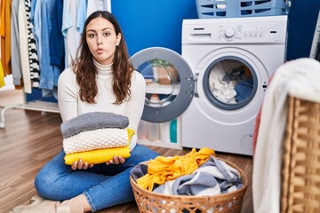 Sticker - Young hispanic woman holding clean laundry making fish face with mouth and squinting eyes, crazy and comical.