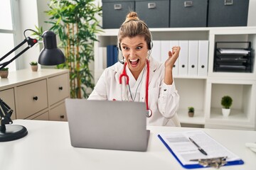 Poster - Young doctor woman wearing doctor uniform working using computer laptop celebrating victory with happy smile and winner expression with raised hands