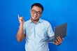 © Krakenimages.com - Chinese young man using computer laptop with a big smile on face, pointing with hand finger to the side looking at the camera.