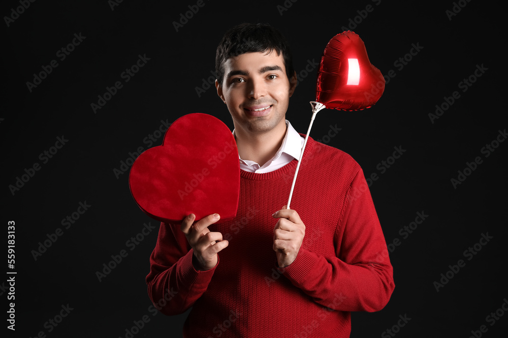 Young man with gift and balloon on black background. Valentine's Day celebration