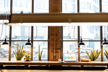 Workplace with laptop and coffee drink on large shared table by the big window at modern coffee shop