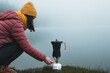 Woman hiker preparing coffee from moka pot coffee maker on camping gas stove by the lake. Adventure, travel, hiking and camping concept