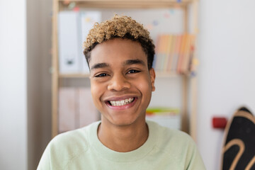 Portrait of smiling young latin american teenage boy looking at camera indoors. POV screen view of millennial man on laptop video call in his room