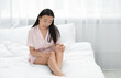 © New Africa - Beautiful young Asian woman applying body cream on leg in bedroom, space for text