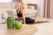 Young Woman In Fitness Clothes Exercising At Home, Focus On Mason Jar Of Smoothie And Apple