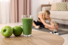 Young Woman In Fitness Clothes Doing Exercise At Home, Focus On Glass Of Smoothie And Apples