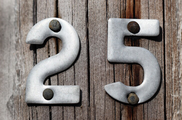 Silver-gray metal numbers two and five (twenty five, 25) nailed to a weathered wood background