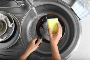 Canvas Print - Woman washing dirty frying pan in sink, above view