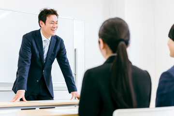 Poster - 会議室で笑顔で話すスーツ姿の先生・講師・教師・ビジネスマンのアジア人男性
