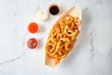 Top Shot Of Curly Fries In A Container With 4 Kinds Of Sauce On A Marble Table