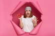 © sementsova321 - Indoor shot of shocked scared young woman wearing white T-shirt and sleeping mask breaking through paper hole of pink background, showing alarm clock, yelling, being late and oversleep.