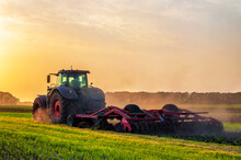 Tractor In The Field Under Sunset Light, Tillage In Spring, Preparation For Sowing. High Quality Photo