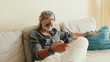 © Andrii Nekrasov - Close-up of the hand of an elderly man with remote control, changes channels while sitting on the couch at home