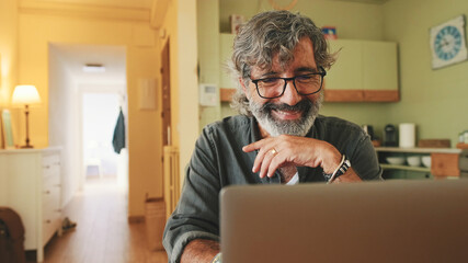 Senior working on laptop sitting in home kitchen