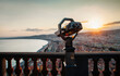 © Cavan Images - Coin-operated binoculars by balusters against cityscape and sky during sunset