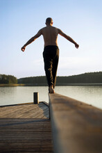 A Man Balances Barefoot On A Rail Of A Wooden Pier At The Shores At One Of The Thousands Of Lakes In The Saimaa Region Of Finlan