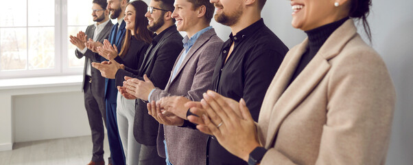 Wall Mural - Happy audience applauding speaker at business conference or corporate team meeting. Group of people in formal suits standing in row in office, clapping hands and smiling. Banner, header background