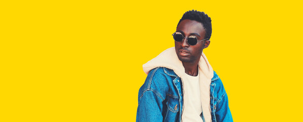 Wall Mural - Portrait of stylish young african man model looking away wearing denim jacket isolated on yellow background, blank copy space for advertising text