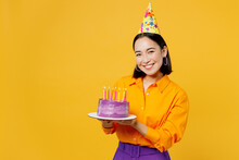 Happy Fun Smiling Young Woman Wearing Casual Clothes Cap Hat Celebrating Holding In Hand Purple Cake With Candles Look Camera Isolated On Plain Yellow Background. Birthday 8 14 Holiday Party Concept.