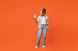 © ViDi Studio - Full body fun young woman of African American ethnicity she wears grey shirt headband hold in hand use mobile cell phone isolated on plain orange background studio portrait. People lifestyle concept.
