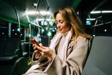 An Attractive Caucasian Woman Using A Smartphone While Riding A Bus In The Night. Young Beautiful Woman Using Public Transportation.