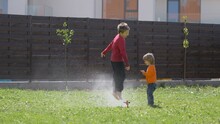 Children Play With Water Sprinkle, Barefoot Brothers Have Fun In Garden