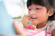 © Prot - Adorable little child Asian girl paints her mouth with pink children heads and looks in the mirror. A child plays at home in a toy beauty salon. Increase learning development for preschoolers.