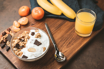 Granola cereal oatmeal with white yogurt, chocolate, banana fruit and nuts in a bowl on dark wooden board