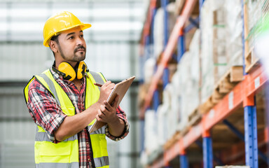 Asian handsome professional male worker holding board, checking shipping stocks in storage, warehouse or factory for delivery, wearing safety hat. Commercial Industry Business Concept.