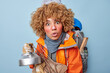 Leinwanddruck Bild - Photo of shocked curly haired woman carries kettle and wood applies protective facial cream on frozen skin poses with rucksack has camping trip isolated over blue background. Hiking and backpacking