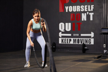 Wall Mural - athletic young woman doing exercises with battle rope in the gym