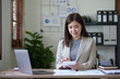 © amnaj - Beautiful Asian businesswoman using her laptop enjoying work, taking notes, reviewing work done.
