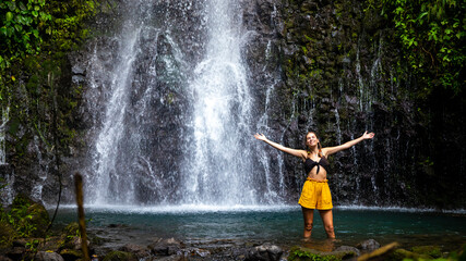 A beautiful girl spreads her arms while standing under a tropical waterfall in Costa Rica; swimming in a hidden waterfall in the rainforest; don jose waterfalls