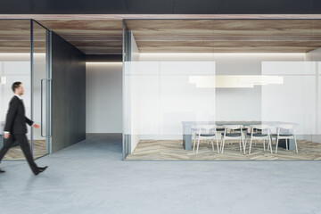 Poster - Businessman walking on concrete floor by stylish conference rooms with minimalistic style furniture on wooden parquet floor behind glass partitions in spacious office hall