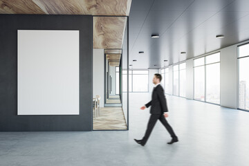 Aufkleber - Walking businessman by blank white poster on black wall background in sunlit modern interior design office with concrete floor, meeting room with wooden decoration and city view background, mock up