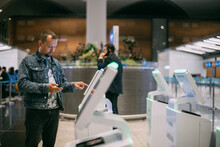 A Male Passenger At The Electronic Check-in Desk In The Departure Area Of The Modern Airport Terminal.